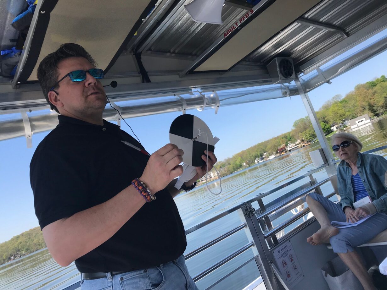 Chris L. Mikolajczyk, CLM, demonstrates to floating classroom participants how to use a Secchi Disks to determine the depth to which light is able to penetrate the water’s surface.