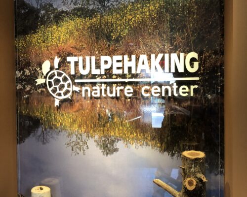 Photo of Tulpehaking Nature Center Sign with name of centern and photo of wetlands in background